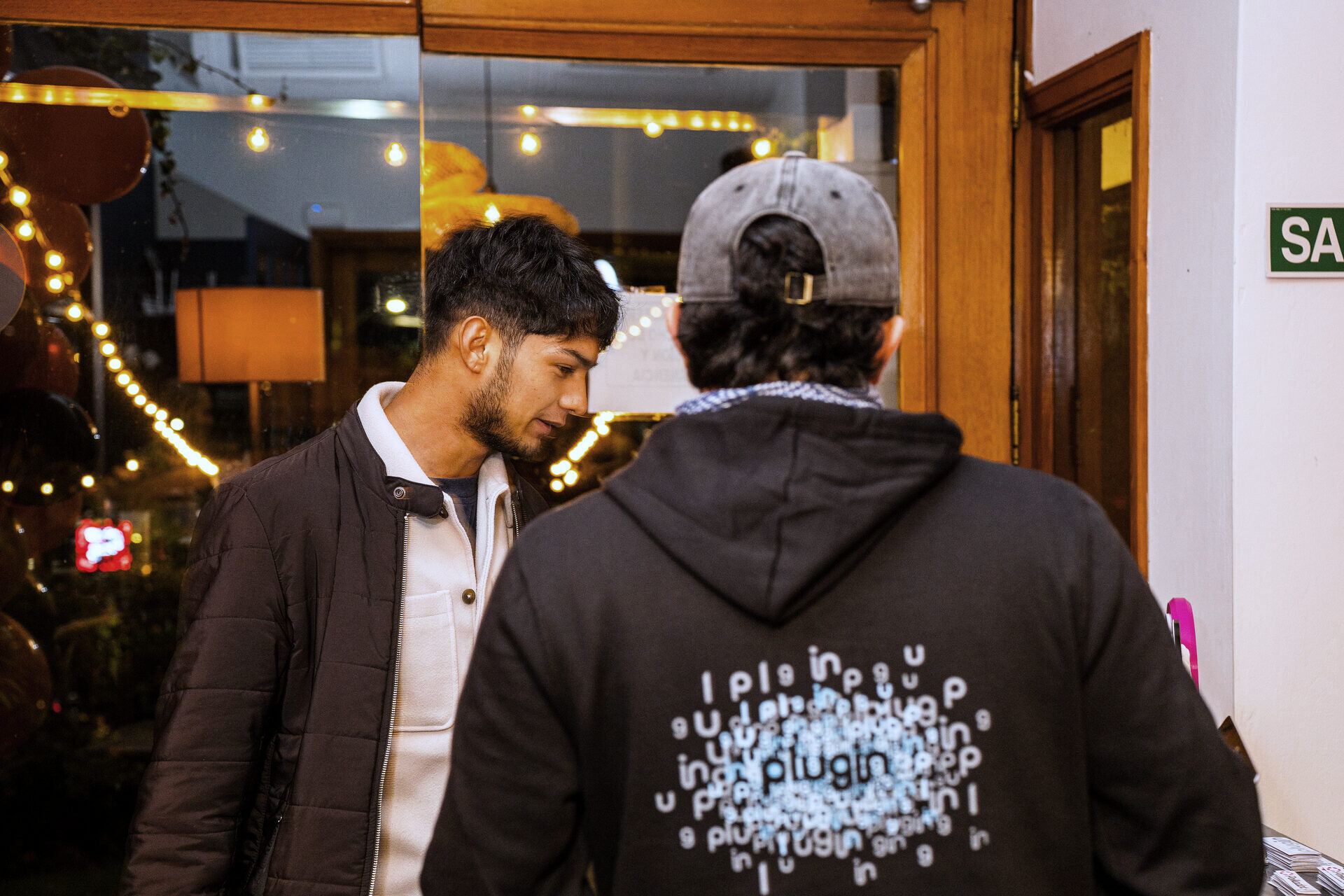 A guest seen from behind in a Plugin hoodie among warm lights.
