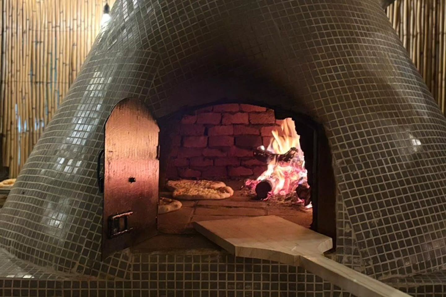 Horno de barro a leña con fuego encendido y una pizza cocinándose.